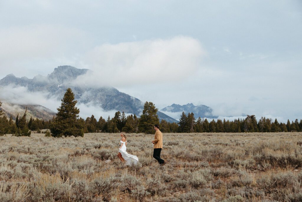 groom playfully chasing bride through a sagebrush field in grand teton national park after their wedding