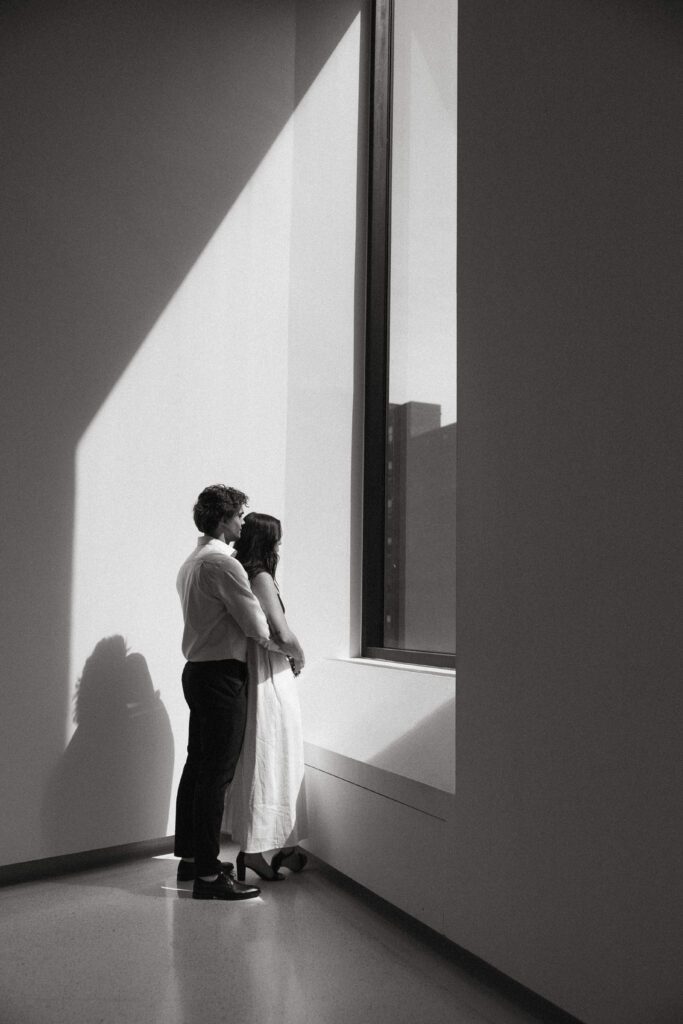 engagement photos of a couple standing by a window at carnegie museum of art taken by pittsburgh engagement photographer