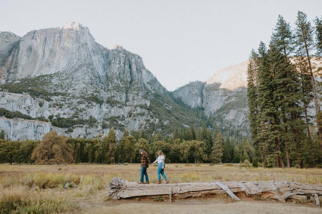 couple walking across log in yosemite national park taken by yosemite engagement photographer