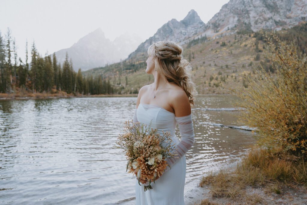 Bride standing in front of string lake holding her bouquet in Grand Teton National Park.