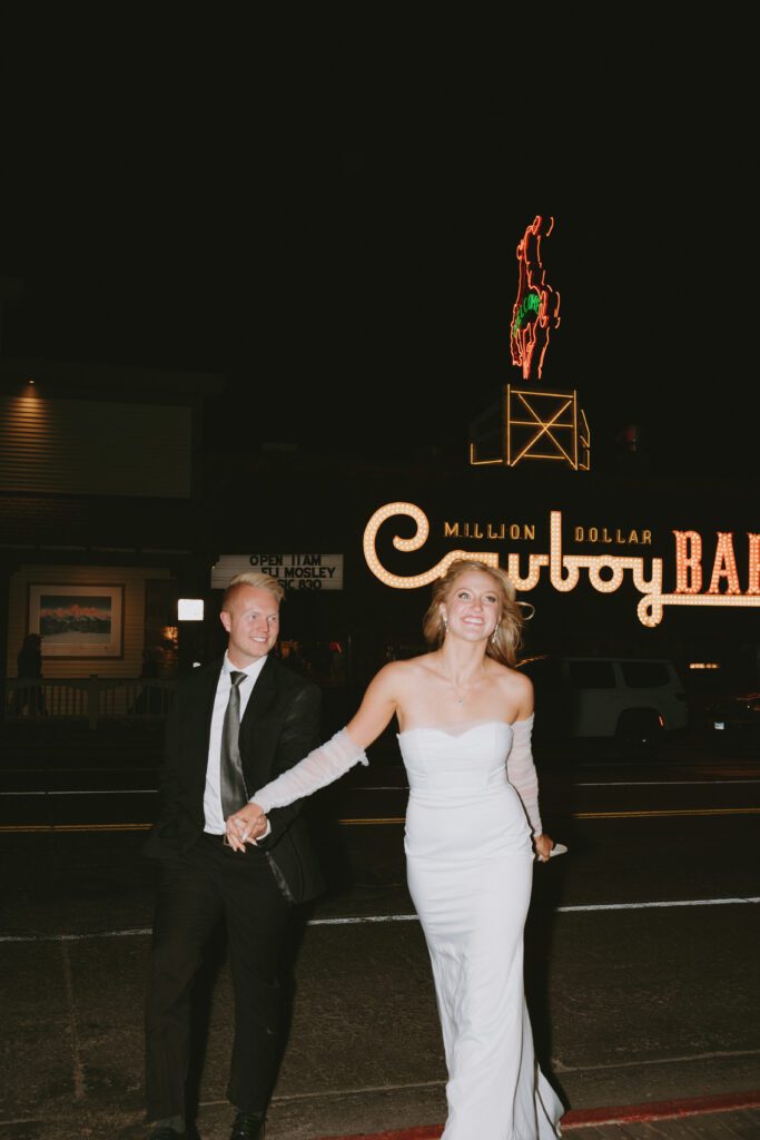 couple walking across the street in front of the million dollar cowboy car in wedding attire