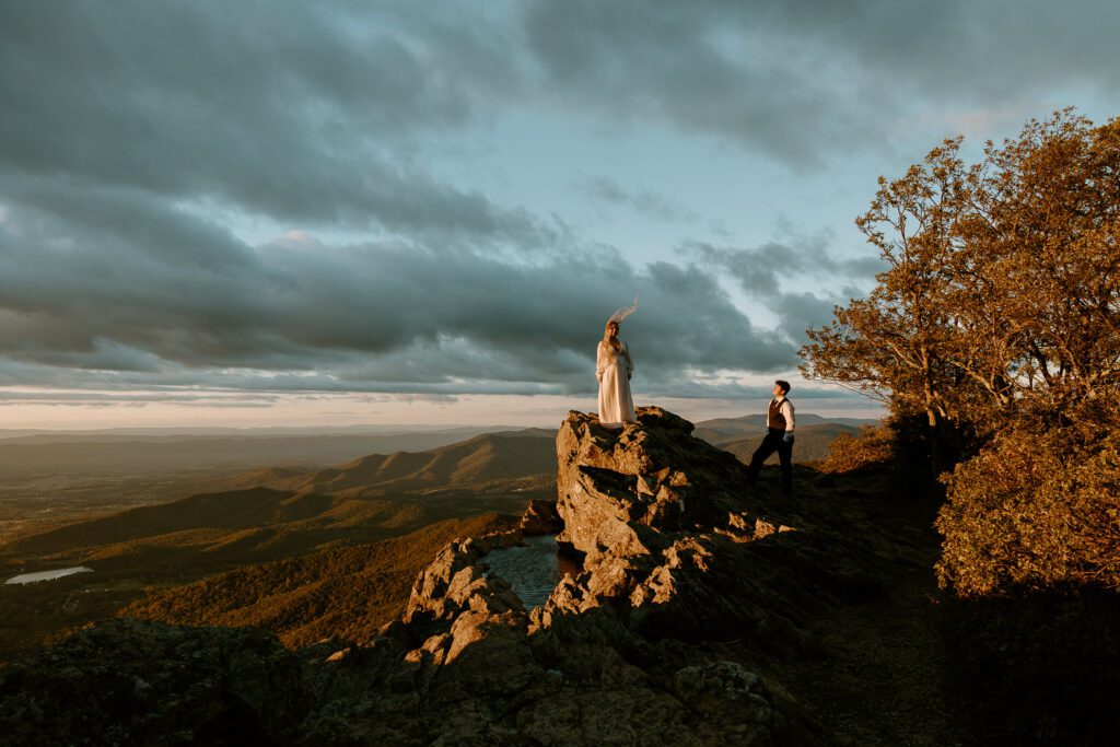 Dramatic scene of couple standing on mountaintop at sunset during a hiking elopement in Shenandoah.