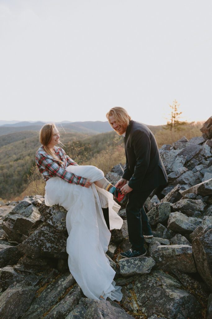 bride and groom laughing while groom ties her hiking book in shenandoah